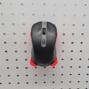 May include: A black and gray wireless computer mouse with a red base. The mouse has a scroll wheel and a button. The word "INMOTION" is printed on the base. The mouse is mounted on a white pegboard.
