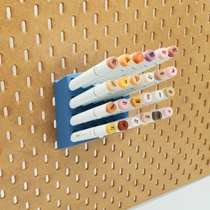 May include: A blue wall-mounted organizer with a grid of holes holds a collection of white and brown markers. The markers are arranged in rows and are labeled with numbers and letters. The text "Craftable" is visible on the organizer.