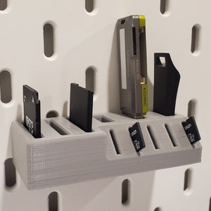 May include: A gray plastic wall-mounted organizer with six slots for storing memory cards. The organizer has a label that says "Micro SD" and "SDMMC".