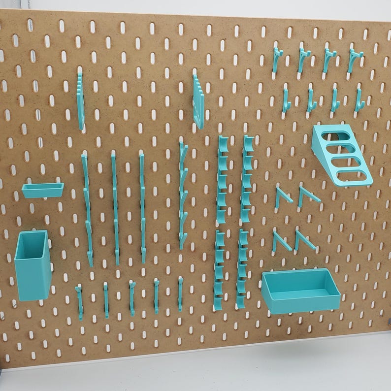 Puede incluir: Un tablero de clavijas con varios ganchos, estantes y organizadores de color turquesa. El tablero de clavijas est&aacute; hecho de madera y tiene un color marr&oacute;n claro.