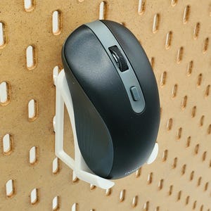 May include: A white plastic mouse holder mounted on a pegboard wall. A black wireless mouse is attached to the holder.