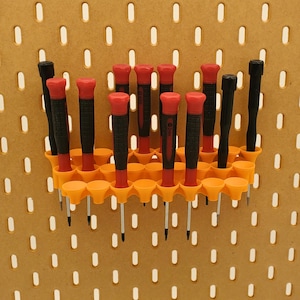 Może przedstawiać: Organizer ścienny z 14 miejscami na wkrętaki. Organizer jest wykonany z pomarańczowego plastiku i ma wzór plastra miodu. Wkrętaki są czerwone i czarne i mają różne rozmiary.