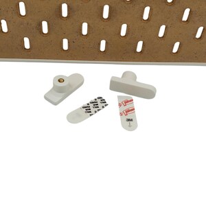 May include: White pegboard accessories, including mounting hardware and adhesive strips. The image shows a white pegboard with several white mounting pegs and adhesive strips with the "Command" brand logo.