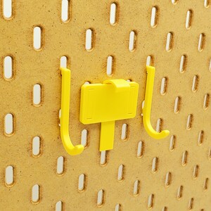 May include: Two yellow plastic hooks with a yellow plastic label attached to one of the hooks. The hooks are mounted on a pegboard.