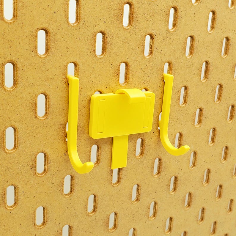 May include: Two yellow plastic hooks with a yellow plastic label attached to one of the hooks. The hooks are mounted on a pegboard.