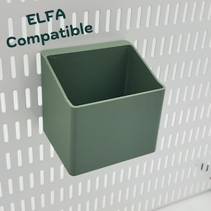 Puede incluir: Un contenedor de almacenamiento de plástico verde compatible con los sistemas ELFA. El contenedor está montado en una tabla de clavijas blanca.