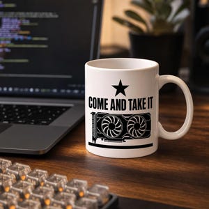 May include: A white ceramic mug featuring a black graphic print. The design includes a five-pointed star, the text "COME AND TAKE IT" in a bold sans-serif font, and a detailed illustration of a dual-fan computer graphics processing unit.