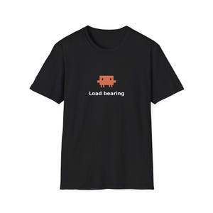 Puede incluir: Una camiseta negra de manga corta con un gráfico pixelado de un personaje cuadrado de color naranja centrado en el pecho. Debajo del gráfico, el texto "Load bearing" está impreso en una fuente blanca sin remates, creando un contraste sencillo.