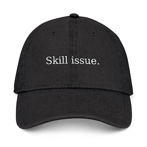 May include: Black baseball cap with the text "Skill issue." The cap has a curved brim and a fabric strap closure at the back. The text is in a simple, sans-serif font.