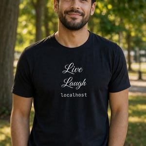 Op de afbeelding: Zwart t-shirt met de woorden "Live Laugh localhost" in een wit scriptlettertype. Het shirt wordt gedragen door een persoon met een baard, die buiten staat voor een vage groene achtergrond.