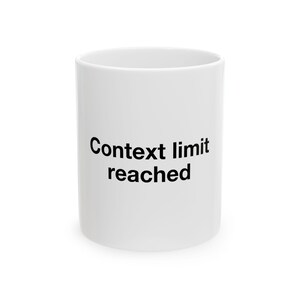 May include: A white ceramic mug featuring the black text "Context limit reached" printed on the front. The mug has a cylindrical shape with a smooth, glossy finish and a simple, clean design, showcasing the bold lettering clearly against the white.