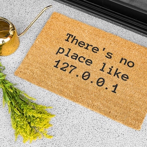 May include: A brown coir doormat with the text "There's no place like 127.0.0.1" in black lettering.