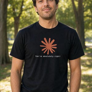 May include: A black short-sleeved t-shirt featuring a rust-colored sunburst graphic centered on the chest. Below the graphic, the text "You're absolutely right!" is printed in a small, white, sans-serif font. The shirt has a crew neckline.