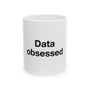 May include: A white ceramic mug featuring the black text "Data obsessed" printed in a simple sans-serif font on the front. The mug has a smooth, cylindrical body with a clean finish, providing a clear view of the bold lettering against the white.