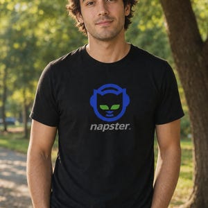 May include: A black t-shirt with a blue and green logo of headphones and the word "napster." The shirt is worn by a person with brown hair, standing outside with a blurred green background.