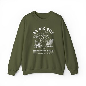 Peut inclure: Sweat-shirt vert olive avec un motif blanc repr&eacute;sentant un cornichon portant un chapeau de cowboy, un lasso, de l'ail et des brins de verdure. Le texte sur le sweat-shirt se lit "NO BIG DILL" et "MINI GARLIC DILL PICKLES WILD WEST PICKLE CO."