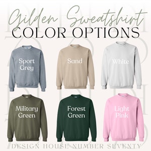 Peut inclure: Pr&eacute;sentation de six sweatshirts Gildan de diff&eacute;rentes couleurs : Gris Sport, Sable, Blanc, Vert Militaire, Vert For&ecirc;t et Rose Clair. Le texte "COLOR OPTIONS" est affich&eacute; au-dessus, avec "DESIGN HOUSE NUMBER SEVENTY" en bas.