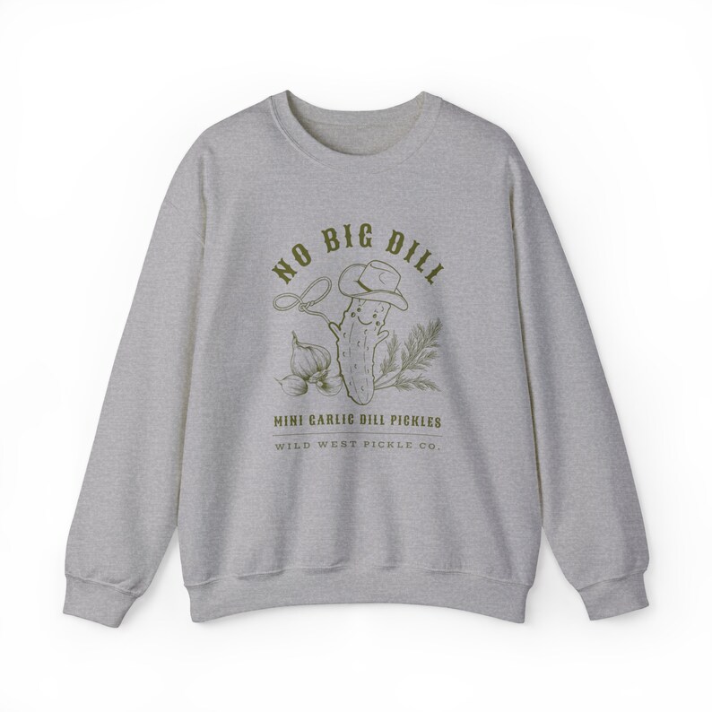 Peut inclure: Un sweat-shirt gris chin&eacute; avec un motif vert d'un cornichon souriant portant un chapeau de cowboy, un lasso et le texte "NO BIG DILL". Les mots "MINI GARLIC DILL PICKLES" et "WILD WEST PICKLE CO." sont en dessous.