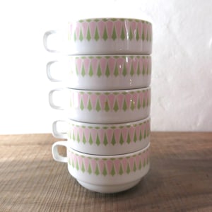 Könnte beinhalten: Ein Stapel von fünf weißen Suppentassen aus Keramik mit einem geometrischen Muster in Rosa und Grün. Die Tassen stehen auf einer Holzoberfläche.