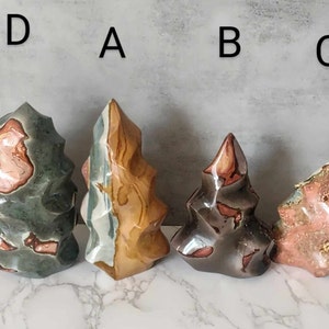 May include: Four colourful, freeform, polished, tree-shaped, agate stones. The stones are arranged from left to right, labelled D, A, B, and C.