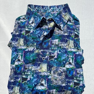May include: Folded button-down shirt with a vibrant abstract pattern in shades of blue, green, and white. The shirt features a contrasting patterned collar and cuffs. The design includes a button-down front and short sleeves.