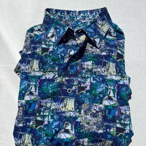 May include: A folded button-down shirt with a vibrant, abstract pattern in shades of blue, green, and white. The design includes what appears to be sailboat imagery. The shirt has a classic collar and button closure.