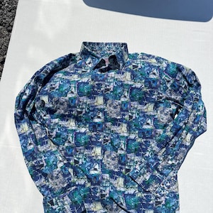 May include: A long-sleeved button-down shirt with a colorful abstract pattern in shades of blue, green, and white. The shirt has a classic collar and buttoned cuffs. The fabric appears to be lightweight.