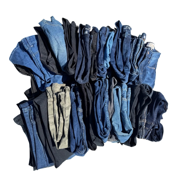 May include: A pile of folded jeans in various shades of blue, black, and a camouflage print. The jeans are neatly stacked, showcasing different washes and styles, from light to dark denim.