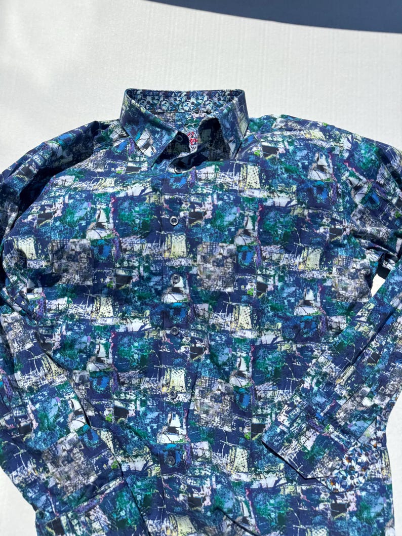 May include: Long-sleeved button-down shirt with a vibrant, abstract pattern in shades of blue, green, and white. The shirt features a classic collar and buttoned cuffs. The overall design gives the shirt a modern and artistic look.