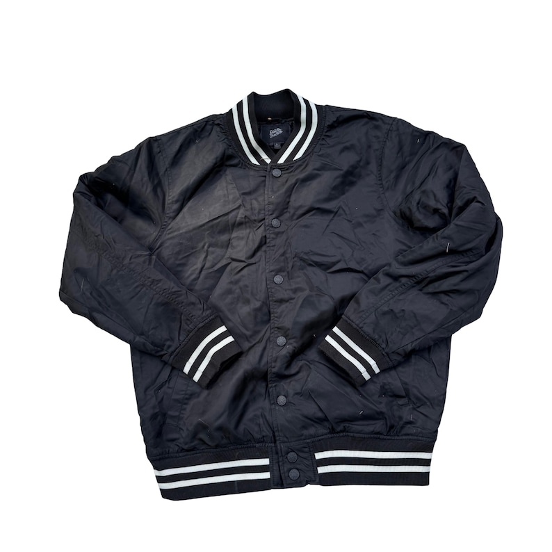 Puede incluir: Chaqueta bomber negra con rayas blancas en el cuello, los pu&ntilde;os y el dobladillo. La chaqueta tiene una parte delantera abotonada y un estilo universitario cl&aacute;sico. La chaqueta est&aacute; hecha de un material ligero.
