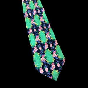 Puede incluir: Una corbata estampada con un diseño floral repetido. La corbata tiene un fondo azul marino oscuro con flores rosas y azules, acentos verdes en forma de hoja y elementos decorativos amarillos.