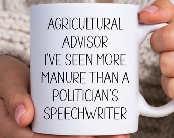 May include: White ceramic coffee mug with black text that reads "Agricultural Advisor I've seen more manure than a politician's speechwriter".