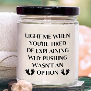 May include: White candle with a black lid and a funny saying: "Light me when you're tired of explaining why pushing wasn't an option."  The candle is surrounded by white towels and pink bath salts.