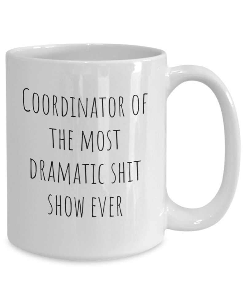 May include: White ceramic coffee mug with black text that reads "Coordinator of the most dramatic shit show ever".