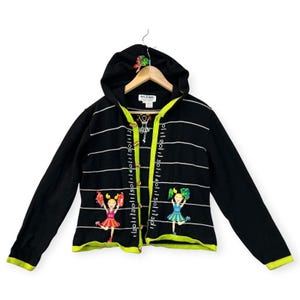May include: Black hooded sweater with white horizontal stripes and neon green trim. Features embroidered cheerleader figures and a scale-like design on the front. The sweater has a button-up closure and a small floral design on the hood.