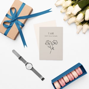 K&ouml;nnte beinhalten: Eine flache Anordnung mit einer Geschenkbox mit blauem Band, einer Karte mit dem Text "I AM more than enough", einer Uhr mit silbernem Armband, einem Strau&szlig; wei&szlig;er Rosen und einer blauen Box mit rosa Macarons.