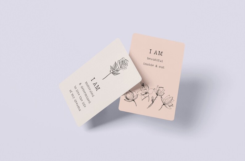 K&ouml;nnte beinhalten: Zwei Affirmationskarten mit floralen Illustrationen und dem Text "I AM", gefolgt von einer positiven Affirmation. Die erste Karte ist cremefarben mit einer Schwarz-Wei&szlig;-Rosenillustration und dem Text "I AM motivated & determined to live the life of my dreams". Die zweite Karte ist hellrosa mit einer Schwarz-Wei&szlig;-Blumenillustration und dem Text "I AM beautiful inside & out".