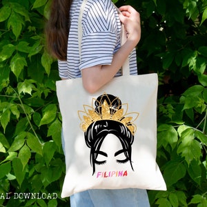 May include: A white tote bag with a black and gold illustration of a woman with a bun and a crown. The text "FILIPINA" is printed in pink, yellow, and blue letters.