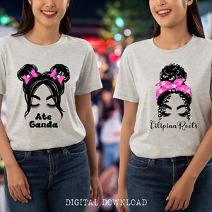 May include: Two gray t-shirts with a black and white illustration of a woman with a bun and a pink headband on one shirt and a woman with pigtails and pink bows on the other. The text "Ate Ganda" is on one shirt and "Filipina Roots" is on the other.