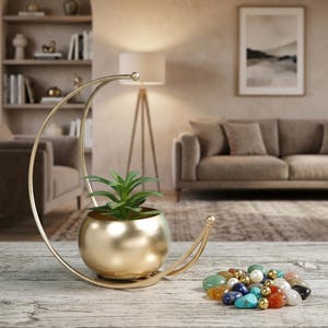Peut inclure: Un support en métal doré en forme de croissant de lune tenant un petit pot rond doré avec une plante succulente verte. À côté du support se trouve une collection de petites pierres décoratives lisses et multicolores et de petites sphères métalliques dorées.