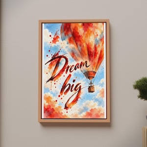 Könnte beinhalten: Ein gerahmter Kunstdruck mit einem Heißluftballon im Aquarellstil, der in einem Himmel aus blauen und orangefarbenen Wolken schwebt. Der Text "Dream big" ist in einer kräftigen, dunkelroten Pinselstrich-Schrift mittig platziert.