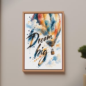 Könnte beinhalten: Ein gerahmter Kunstdruck mit einem Heißluftballon im Aquarellstil in Blau-, Orange- und Gelbtönen. Der Text "Dream big" ist in einer fetten, schwarzen Pinselstrichschrift in der Mitte zu sehen, umgeben von bunten Farbspritzern auf dem Bild.
