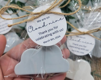 May include: A small, gray cloud-shaped soap bar with a white circle tag attached. The tag reads "We are on Cloud nine Thank you for celebrating with us! March 9th, 2024".