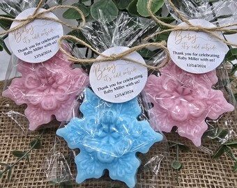 May include: Two snowflake-shaped favors, one blue and one pink, with a white circle tag attached to each. The tag reads "Baby it's cold outside" and includes the date "12/14/2024".