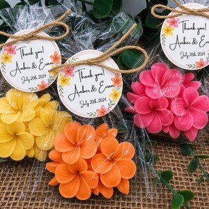May include: Three clear plastic bags containing flower-shaped soaps in yellow, orange, and pink. Each bag is tied with twine and features a round tag printed with "Thank you! Amber & Evan" and "July 20th, 2024" surrounded by colorful floral illustrations.