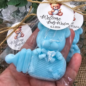 May include: Blue teddy bear shaped soap with a knitted pattern and a bow. The soap is packaged in a clear plastic bag with a brown twine bow and a round white tag with the text "Welcome Baby Weston 6.2.2024".