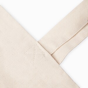 Pode incluir: Close-up das costuras refor&ccedil;adas na al&ccedil;a de uma bolsa de lona de cor natural.