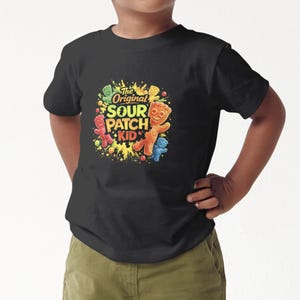May include: Black t-shirt featuring a colorful graphic of Sour Patch Kids. The design includes the text "The Original Sour Patch Kid" with images of the candy characters in red, orange, and blue. The shirt is worn by a child.
