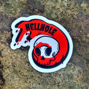 May include: A white sticker with a red and black skull and the text "HELLHOLE" in a red wave.