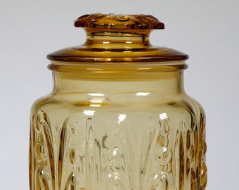 May include: A clear amber glass jar with a lid. The jar has a hexagonal shape and a decorative embossed pattern. The jar is perfect for storing cookies, candy, or other treats.